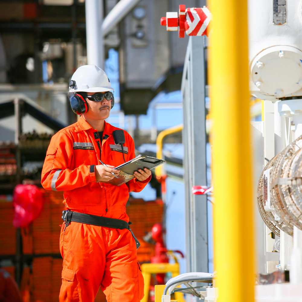 A person wearing PPE, holding a clipboard. Standing next to a machine.