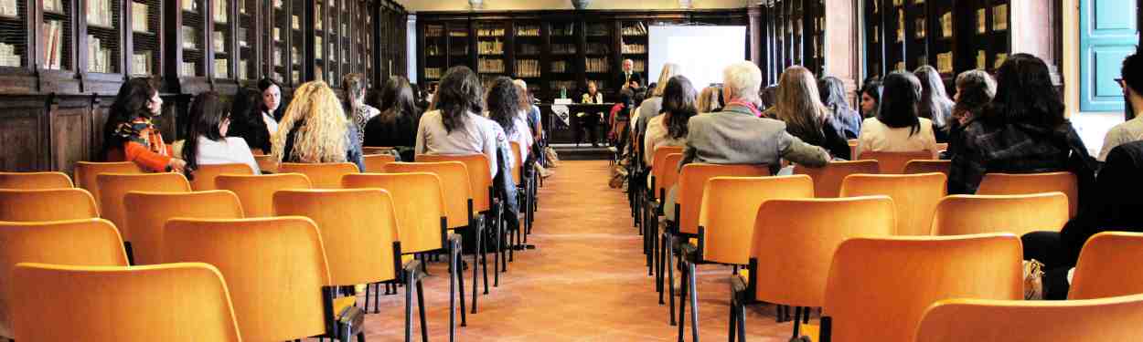 training, a lot of chairs placed in rows, some people sitting in them and at the front is a person teaching the rest.